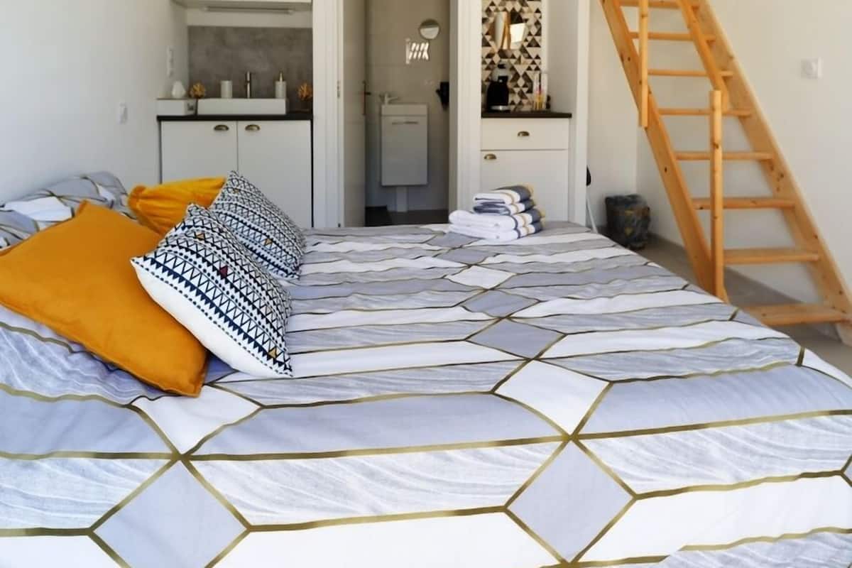 A bedroom with a bed, a staircase, a kitchen, and a bathroom.