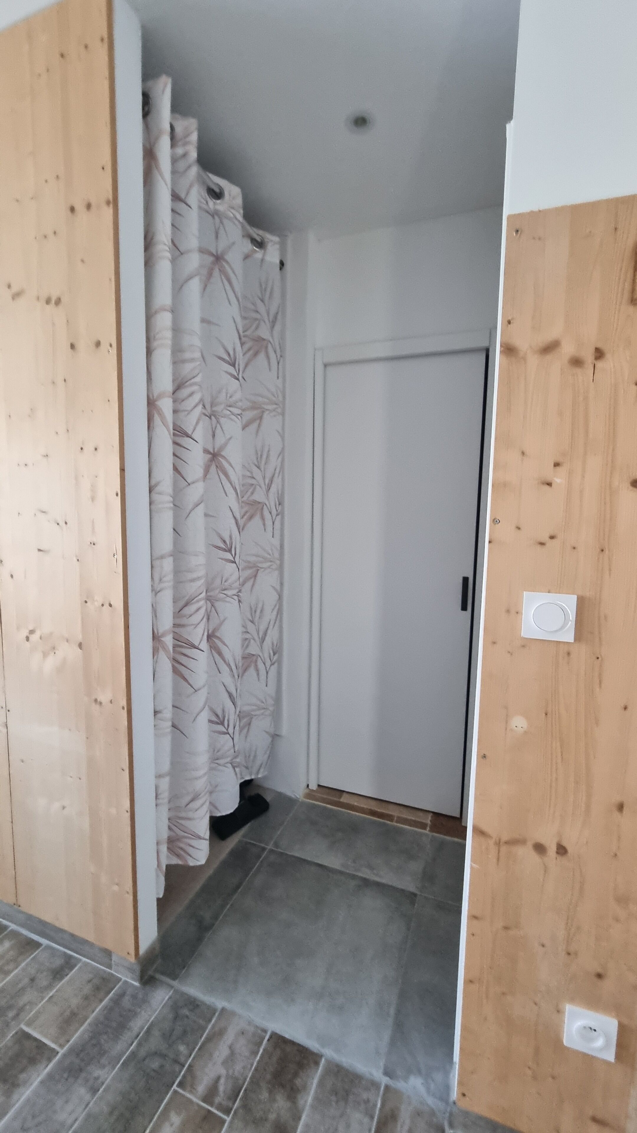 En hall med en dörr av trä, en vit dörr och en duschdraperi med ett lövmönster.