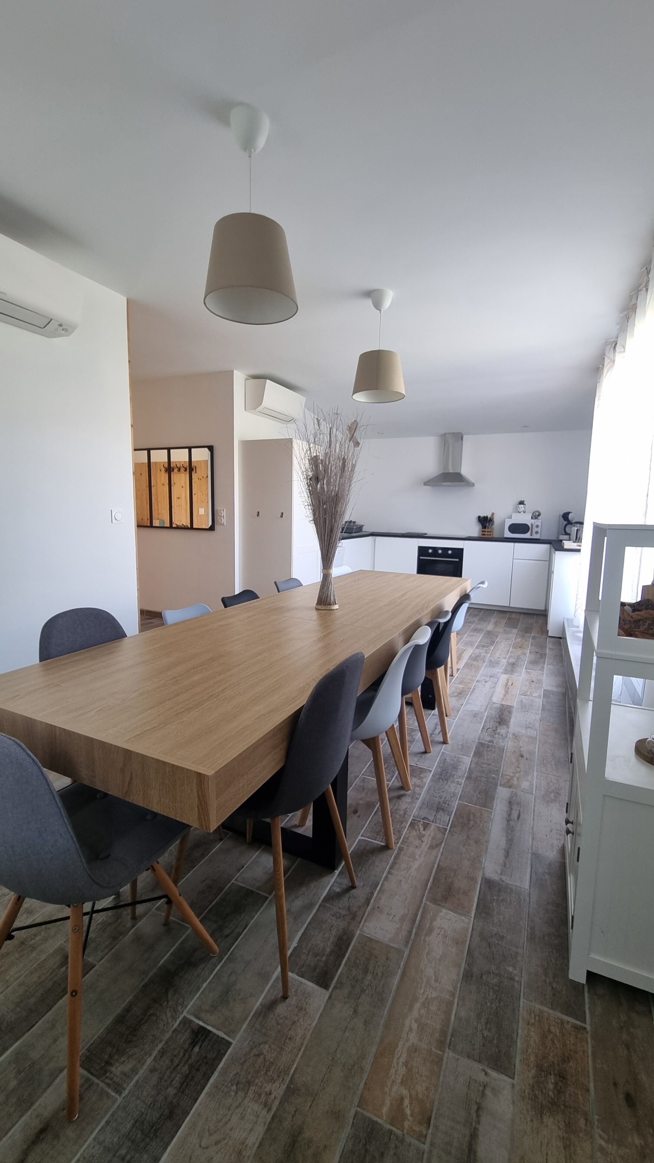 A modern kitchen with white cabinets, a wooden dining table, and pendant lights.