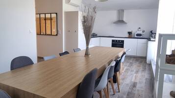 A modern kitchen with white cabinets, a wooden dining table, and pendant lights.