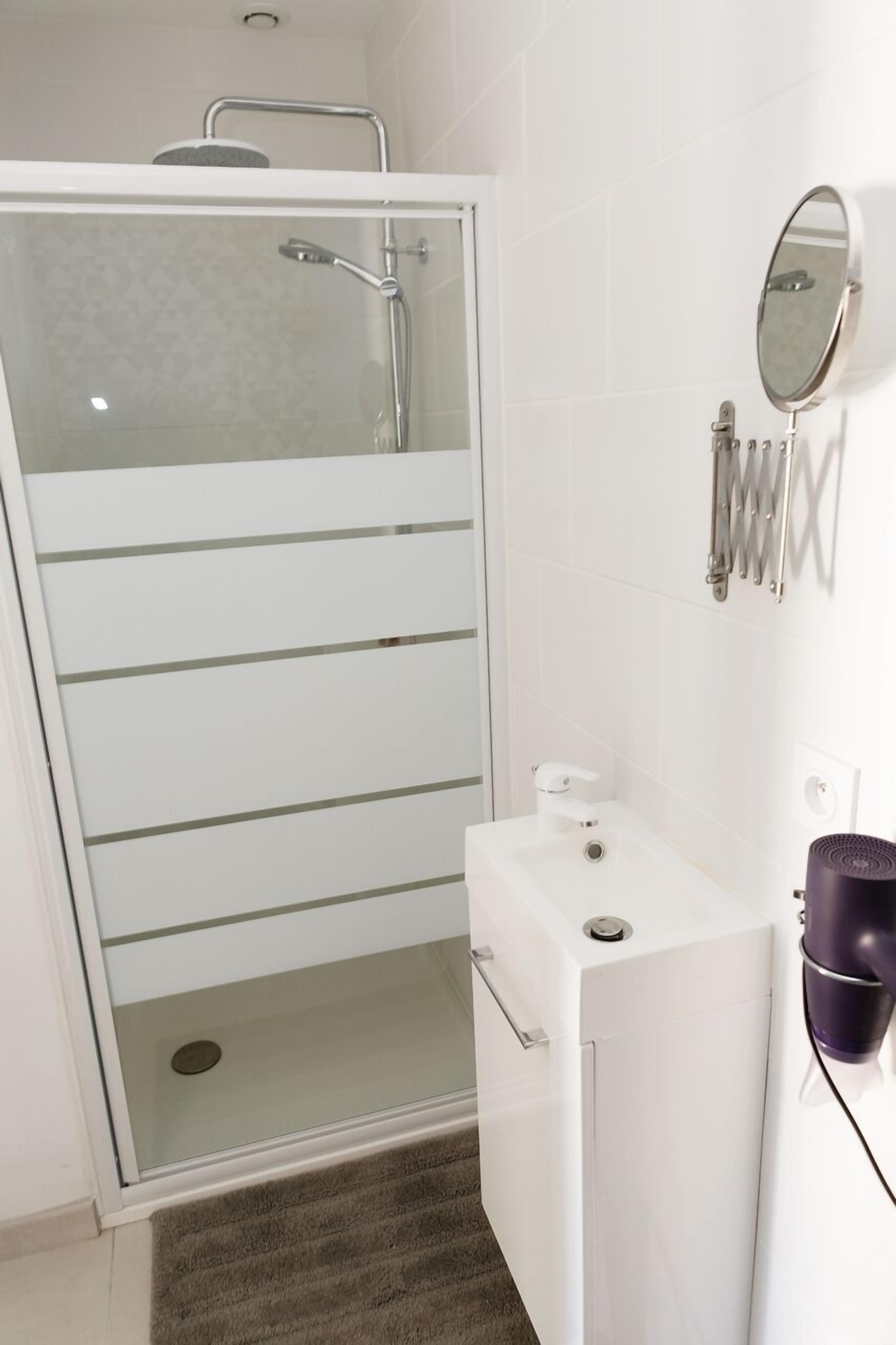 Een moderne badkamer met een douchecabine van glas, een witte wastafel met spiegel en een handdoekrek.