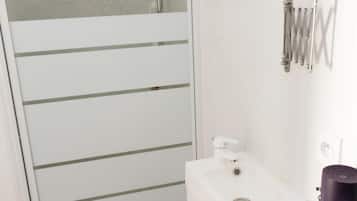Een moderne badkamer met een douchecabine van glas, een witte wastafel met spiegel en een handdoekrek.