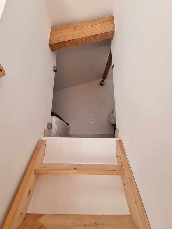 Un ático estrecho y sin terminar, con vigas de madera a la vista y techo blanco.
