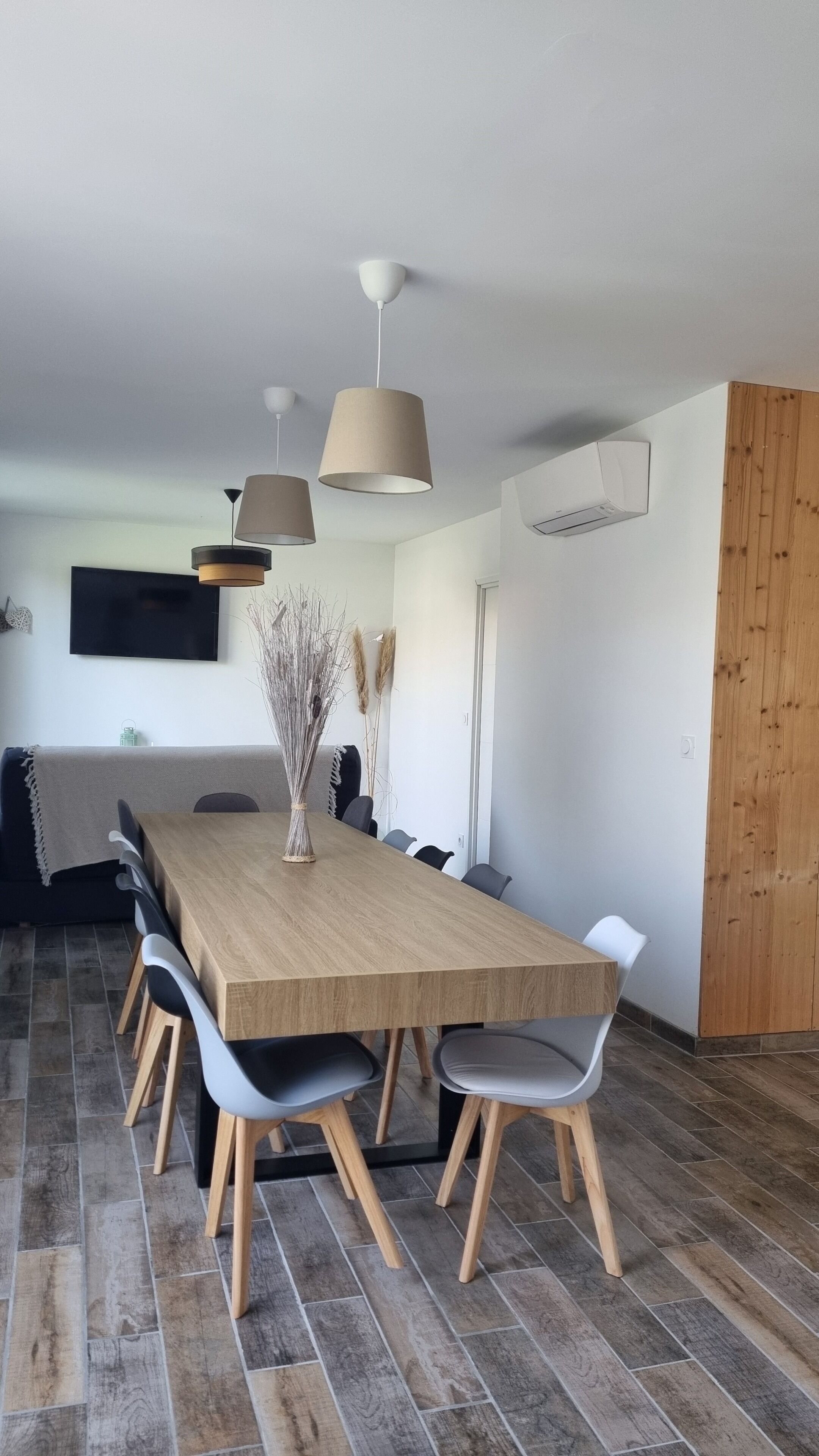Un espace repas moderne avec une table en bois, des chaises grises et des luminaires suspendus.