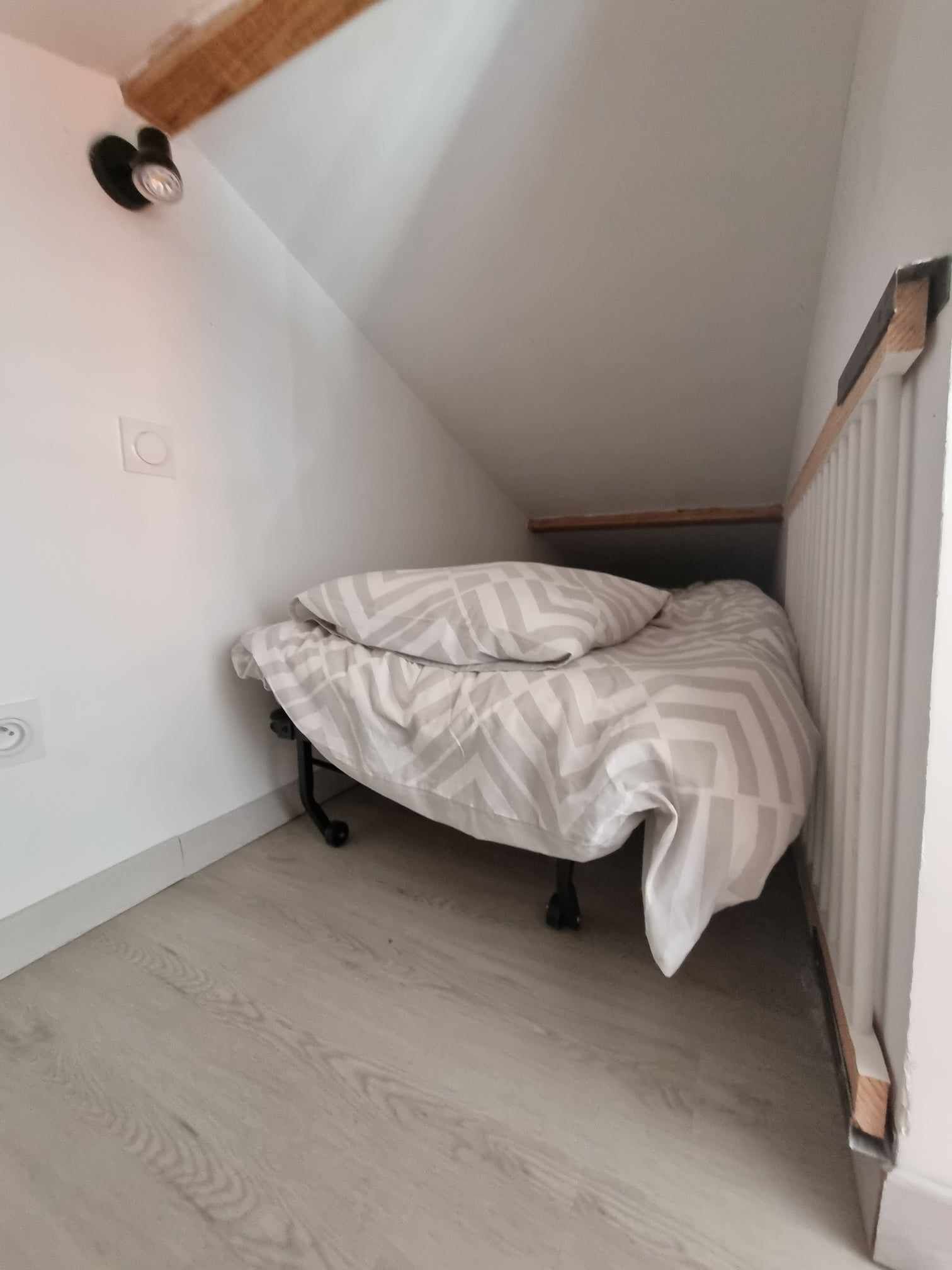 A small, narrow room with a bed in the corner, a radiator, and a wooden beam above the bed.
