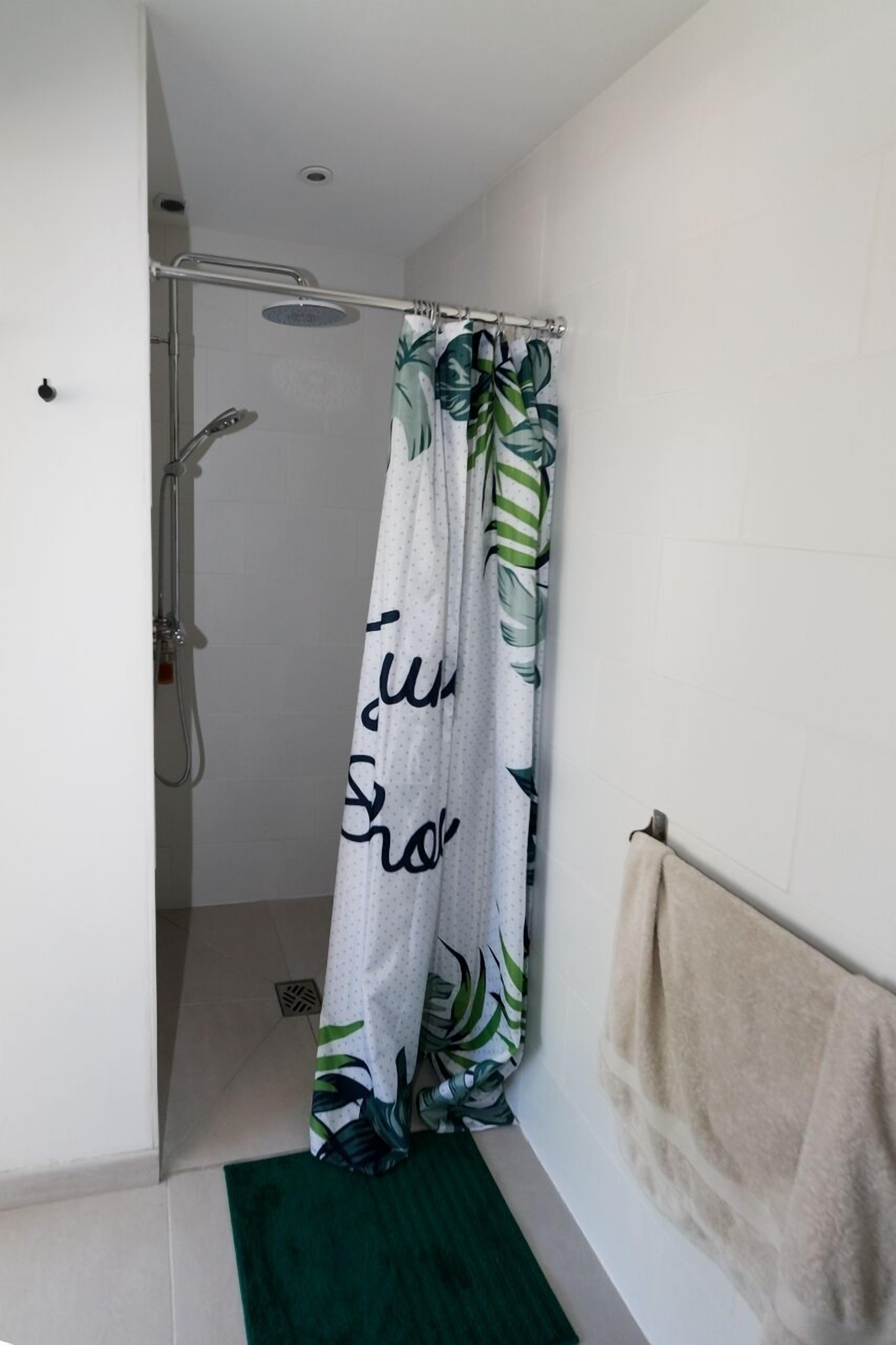 Un área de ducha con cortina blanca decorada con un diseño de hojas tropicales y la frase 'I love shower' en negro.
