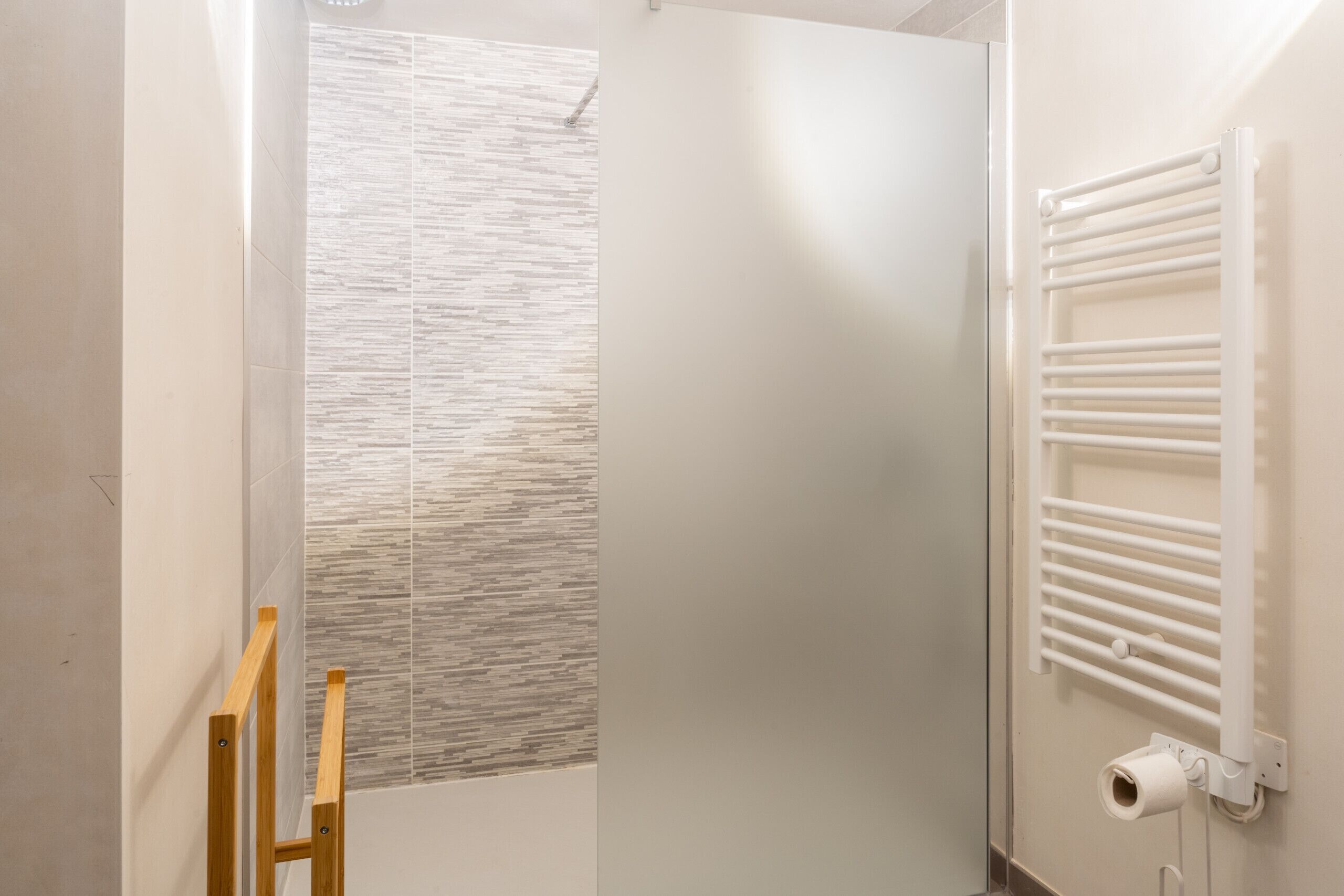A bathroom with a shower, a towel rack, and a wooden ladder.