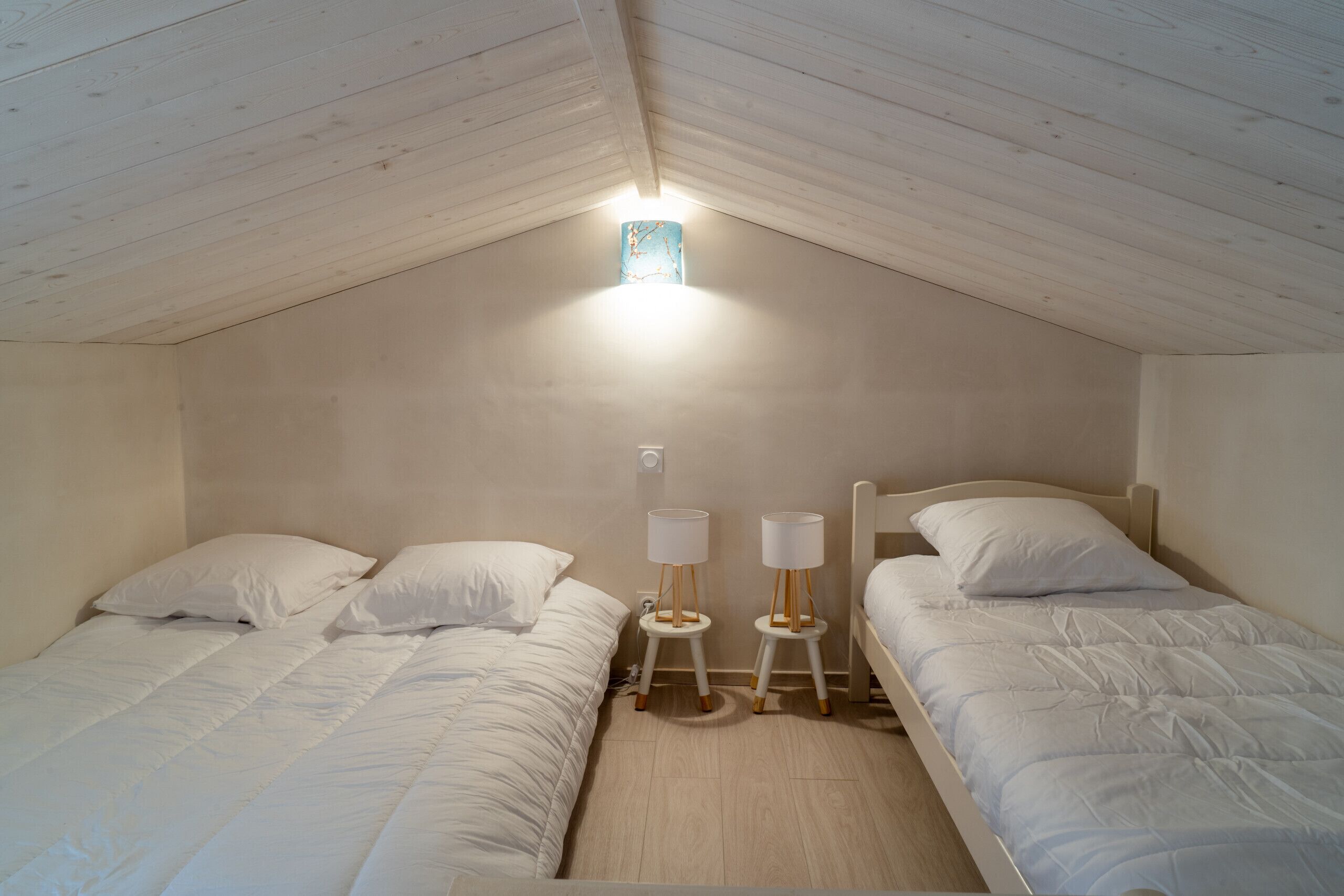Une chambre avec deux lits, un plafond en pente et une petite fenêtre.
