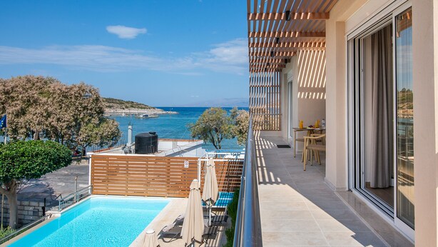 Un balcone con vista sul mare, una piscina e un tavolo con sedie.