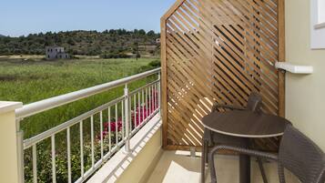Un balcón con una mesa, una silla, un panel de madera y vistas a un edificio y campo a lo lejos.