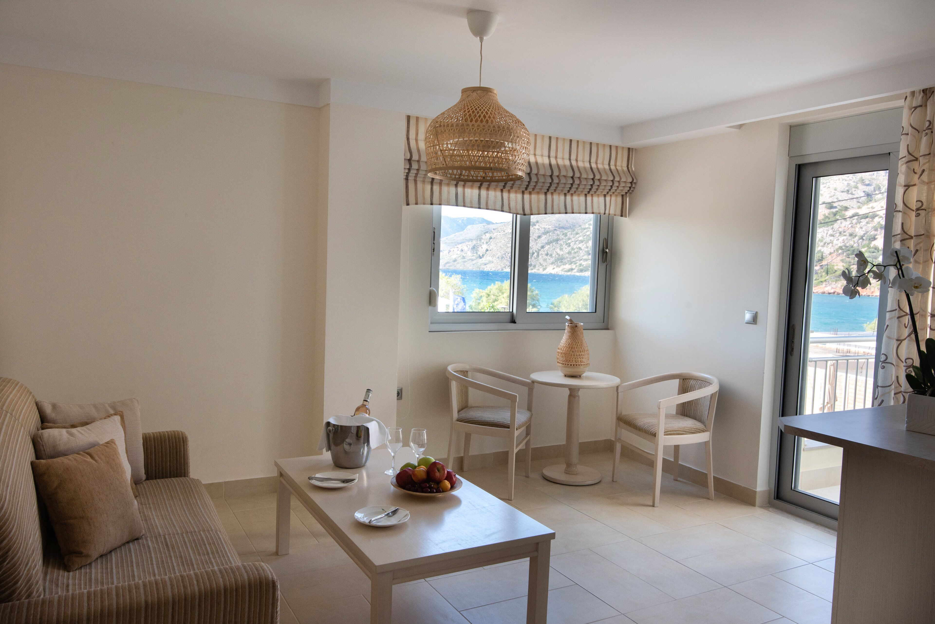 Un salon moderne comprenant un canapé, une table à manger et deux chaises. Une fenêtre offre une vue sur la mer et les montagnes.