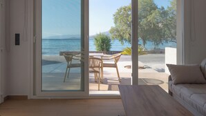 Una stanza con una porta vetrata scorrevole che dà su un balcone con tavolo e sedie, con vista su un corso d'acqua e un albero.