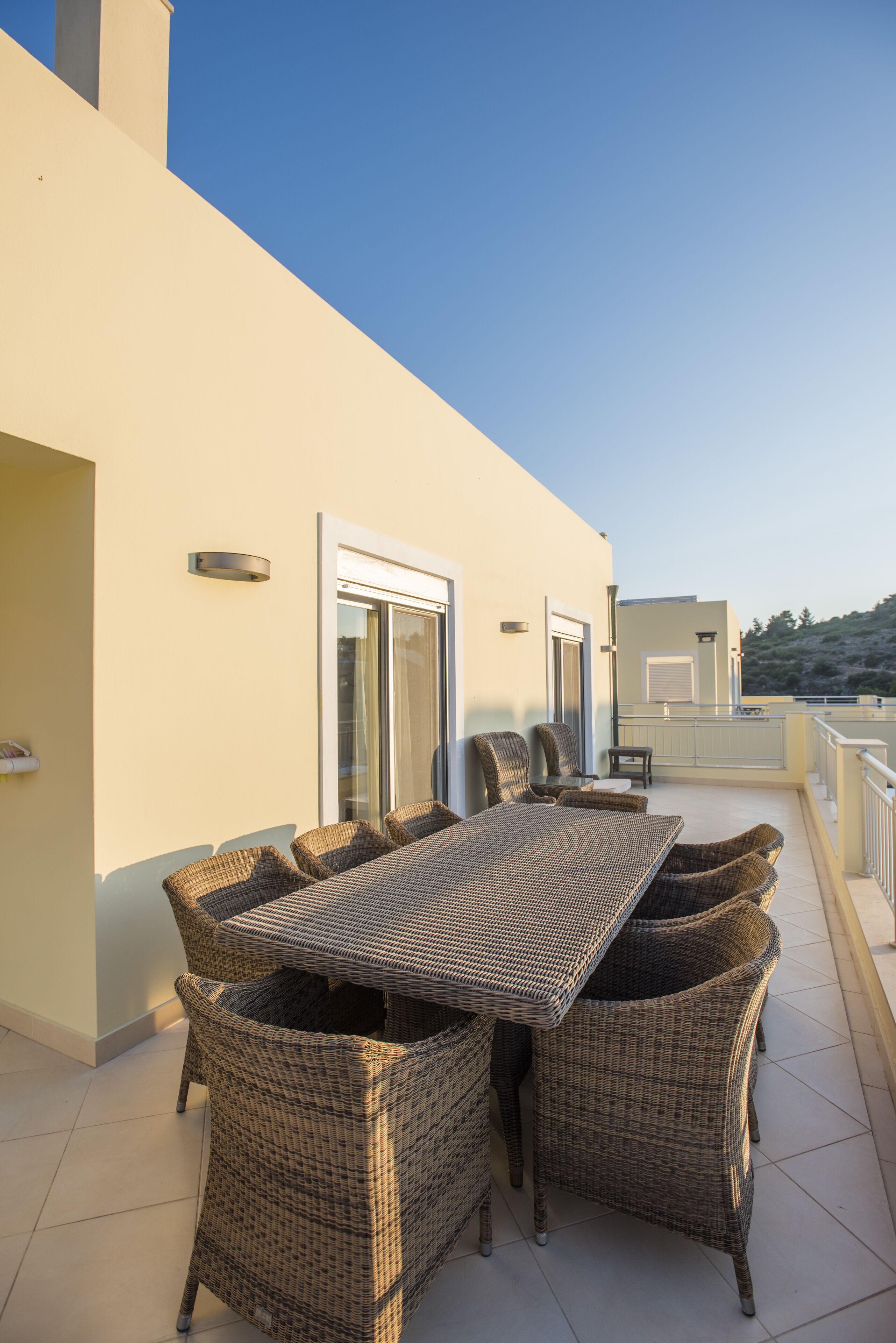 A terrace with a wicker table and chairs, a glass door, and a view of the landscape.