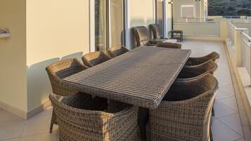 A terrace with a wicker table and chairs, a glass door, and a view of the landscape.