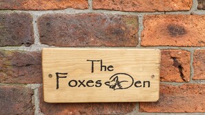 A wooden plaque with the inscription "The Foxes Den" mounted on a brick wall.