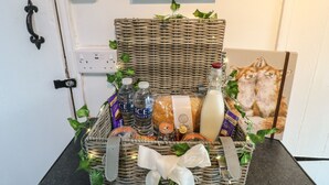A wicker basket with a white ribbon, containing various items like bottles, a candle, and a framed picture of a cat.