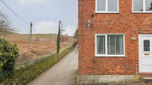 A brick house with a white door and shutters, a stone wall, and a narrow road.