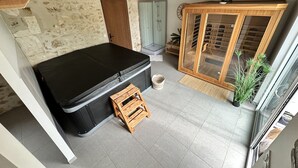 A room with a stone wall, a black sofa, a wooden stool, a glass cabinet, and a potted plant. - Charming gîte "Chez Erwann" 108m2 (Saint-Just)
