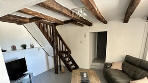 A living room with a wooden coffee table, leather sofa, and a TV on a stand. A staircase leads to an upper level. - Charming gîte "Chez Erwann" 108m2 (Saint-Just)