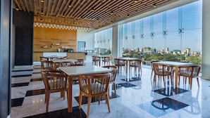 A modern dining area with wooden tables and chairs, a checkered floor, and a city view through large windows.