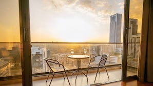 A balcony with two chairs and a table, overlooking a cityscape during sunset.