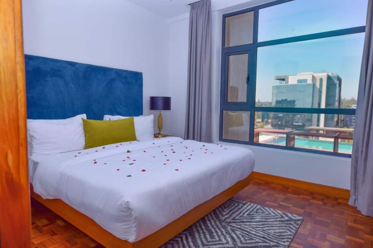A hotel room with a large bed, a view of a swimming pool, and a modern building in the background.