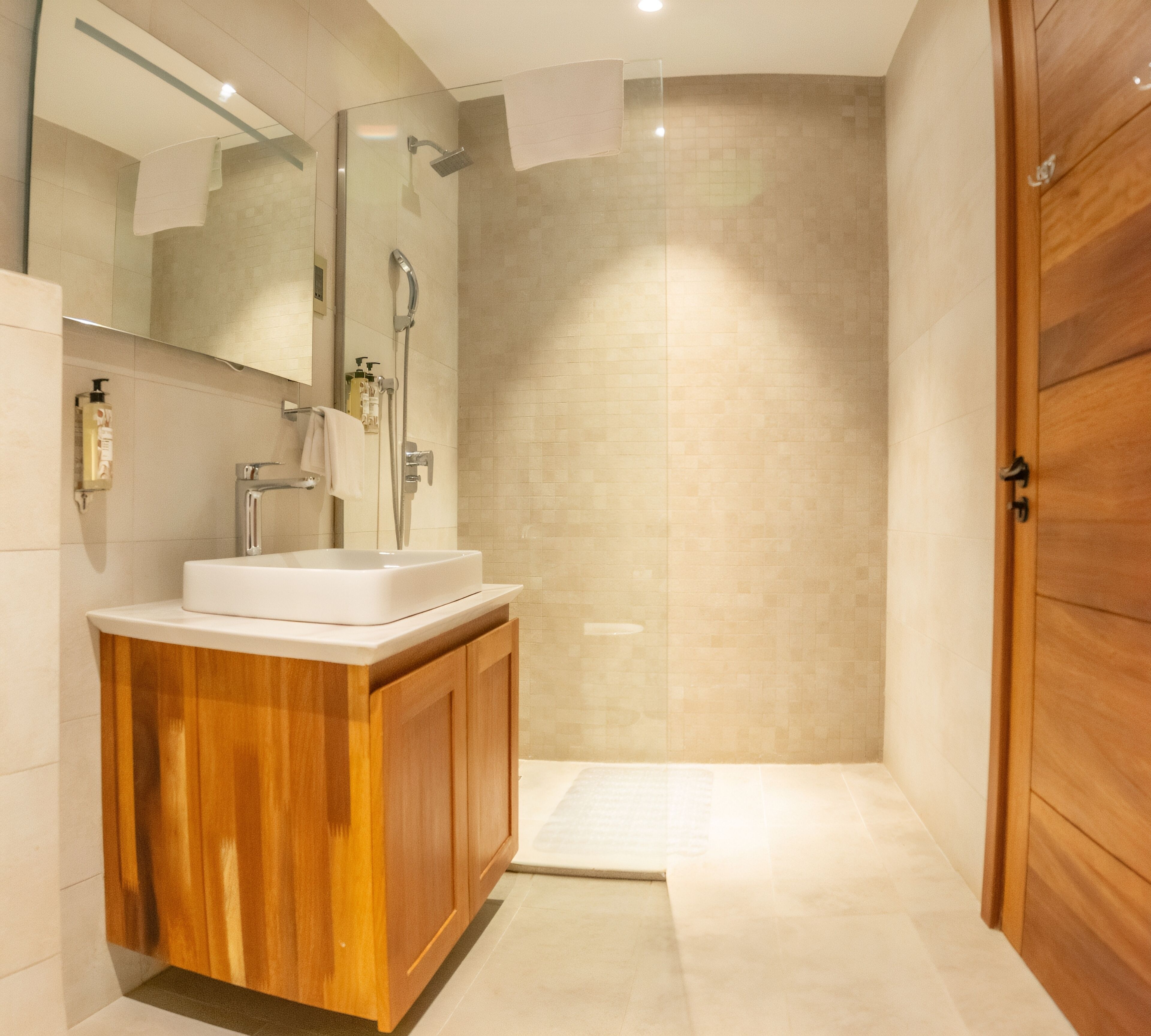 A modern bathroom with a wooden vanity, a glass shower enclosure, and a large mirror.