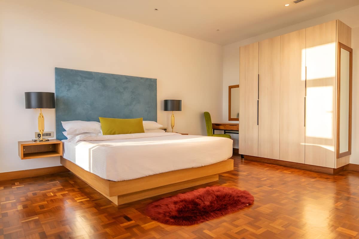 A modern bedroom with a large bed, wooden flooring, a red rug, and a wardrobe.