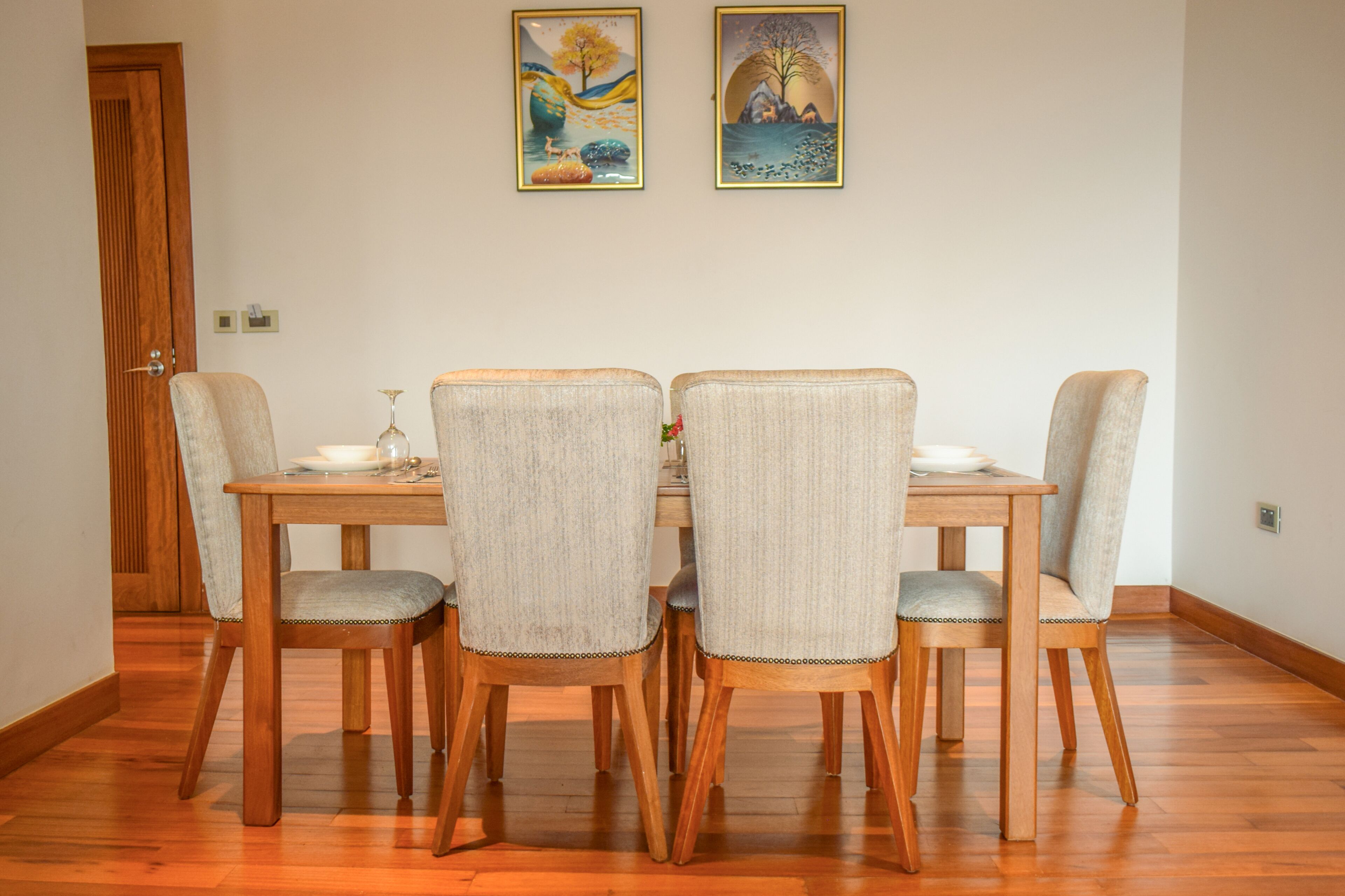 Un comedor con una mesa de madera y cuatro sillas tapizadas. Dos obras de arte enmarcadas adornan la pared sobre la mesa.