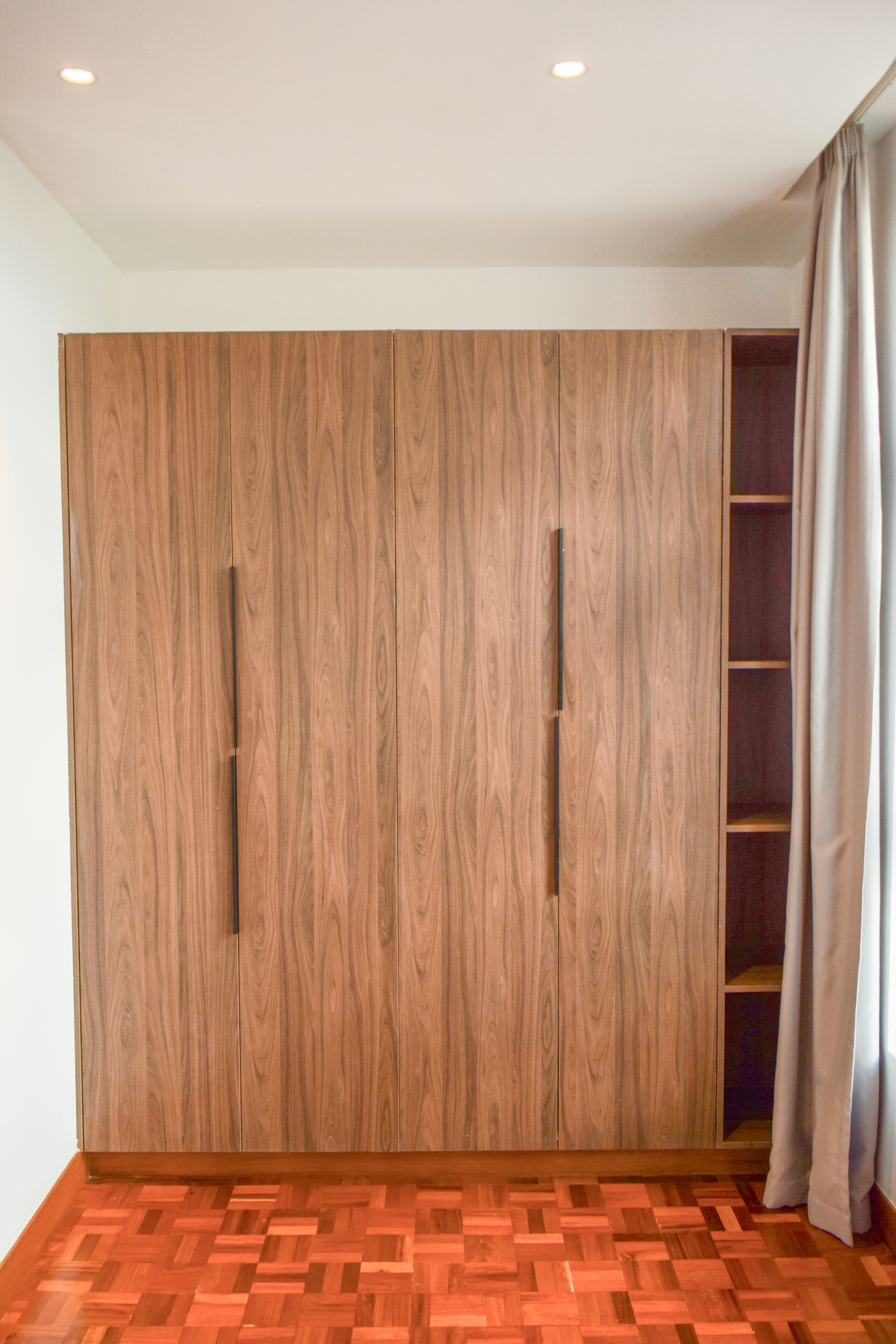 A room with a wooden wardrobe, a herringbone-patterned floor, and a curtain on the right.