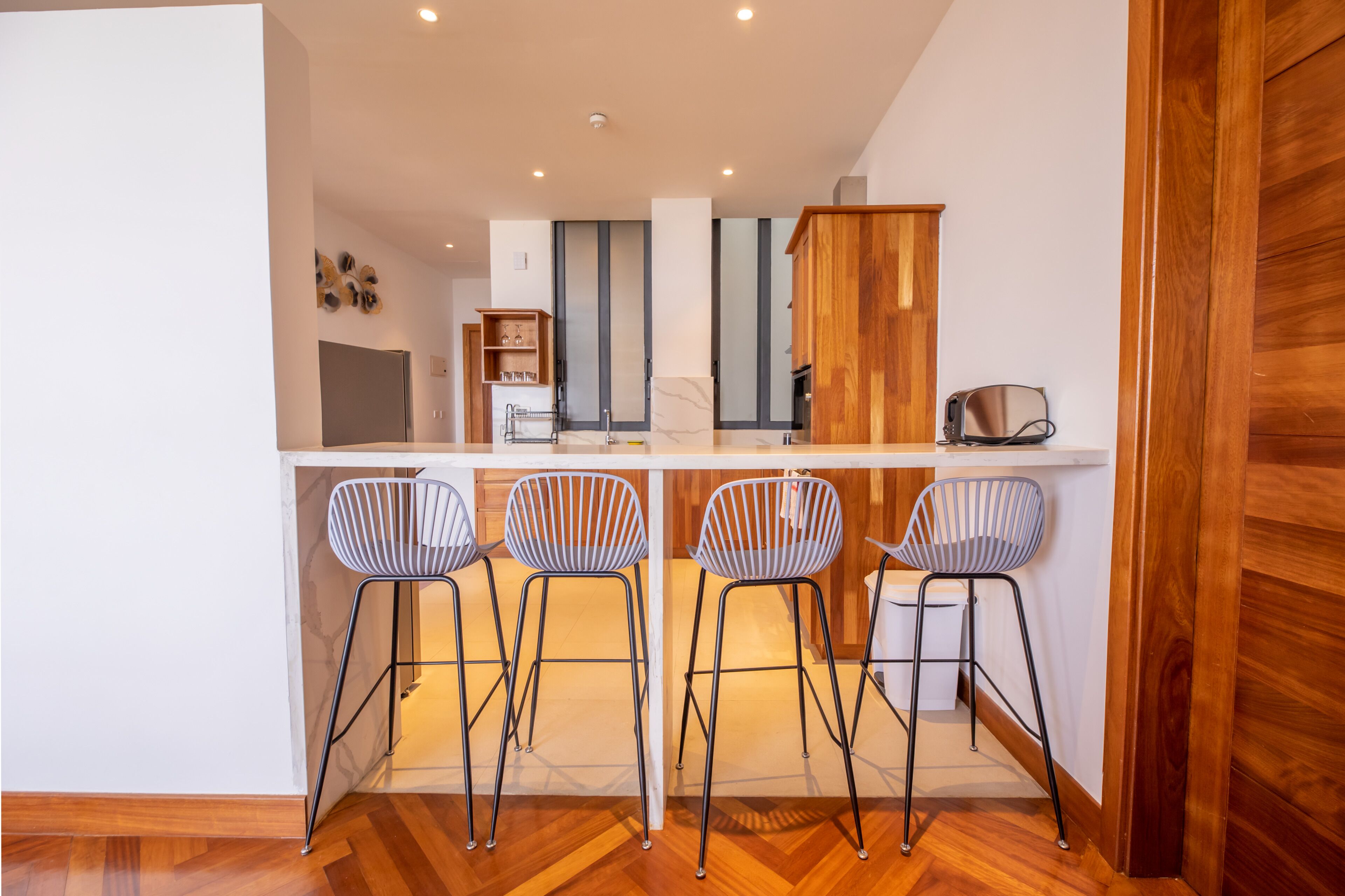 A modern kitchen with a central island, four bar stools, and wooden cabinetry.