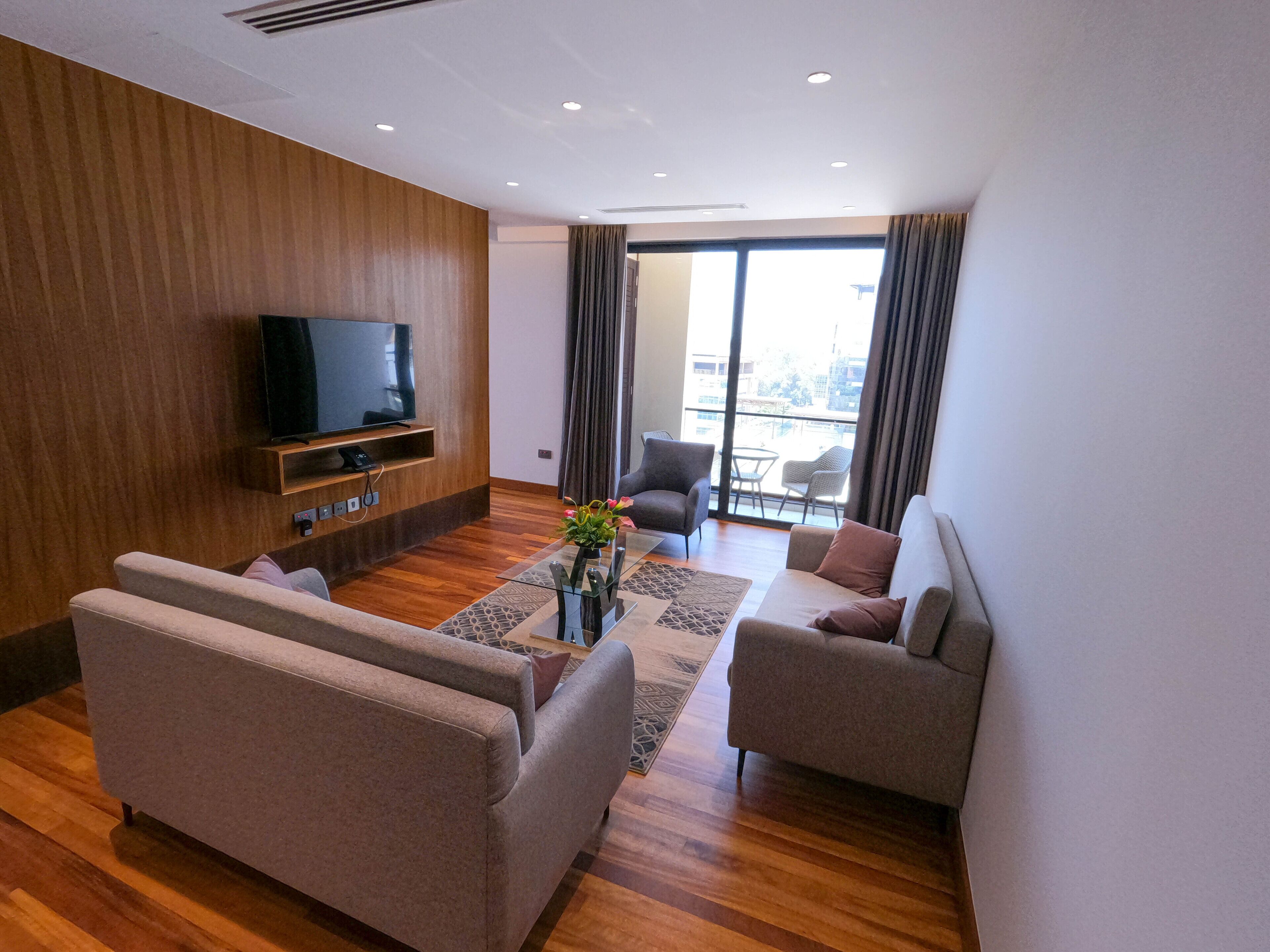 Ein modernes Wohnzimmer mit Flachbildfernseher, zwei Sofas, einem Couchtisch und Blick auf die Stadt durch große Fenster.