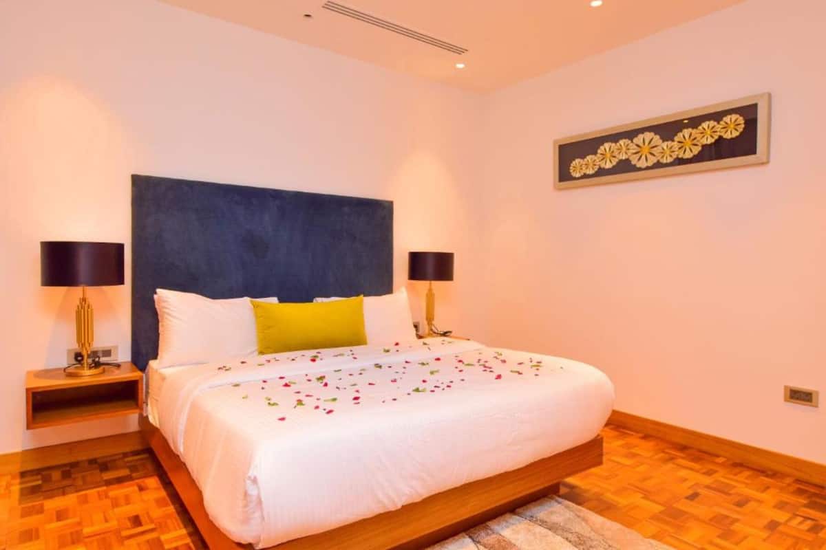 A bedroom with a bed, two bedside tables, a headboard, a wall-mounted artwork, and a wooden floor.