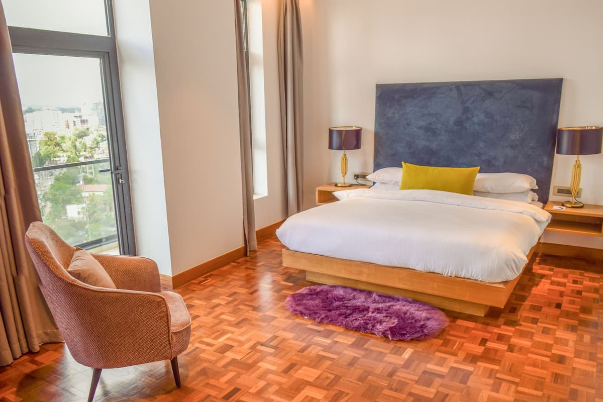 A modern bedroom with a large bed, a chair, a view of the city, and a large window.