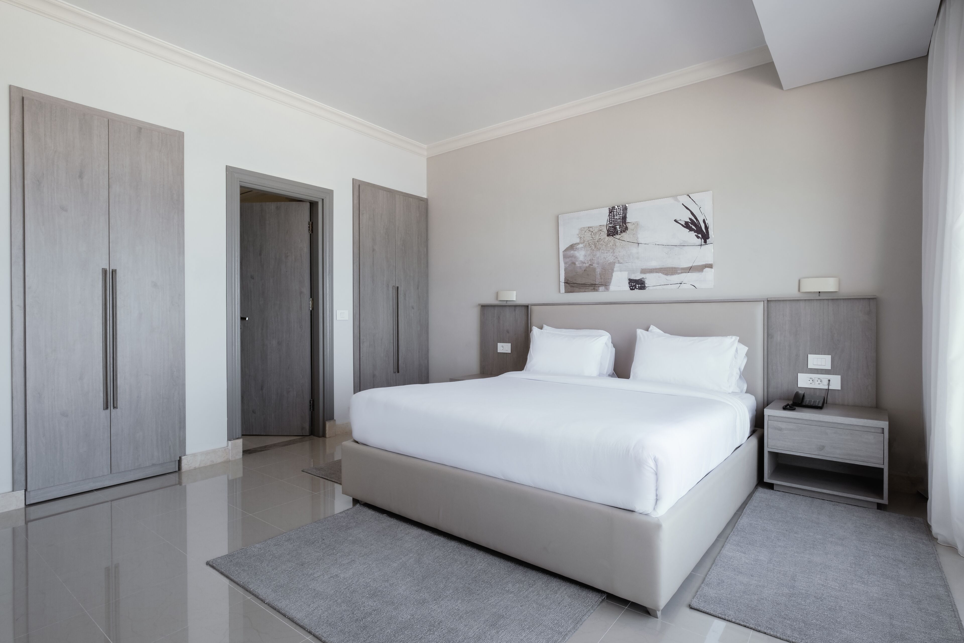 A modern bedroom with a large bed, grey wardrobe, and a bedside table with a lamp.