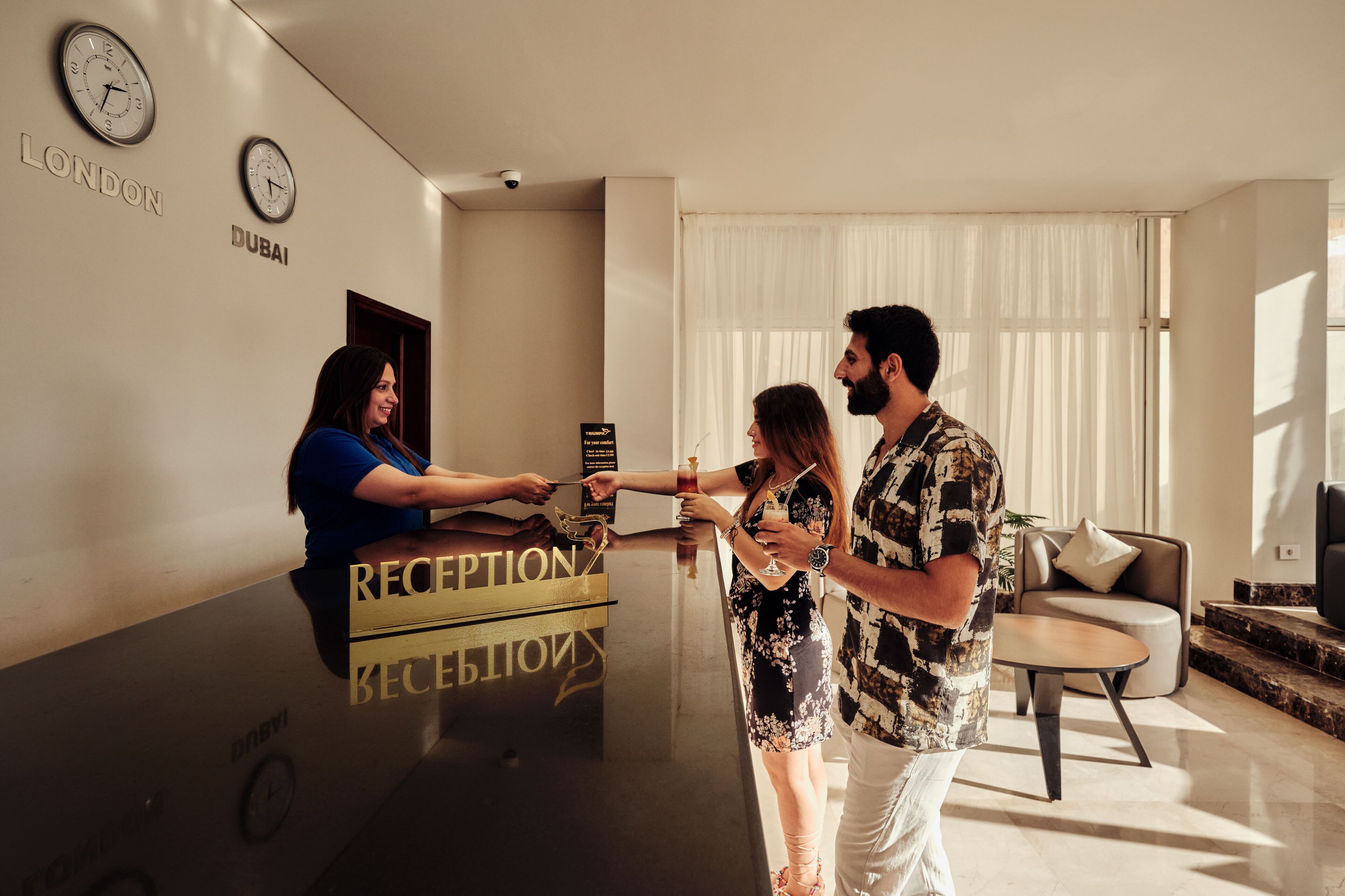 A reception desk with clocks labeled "LONDON" and "DUBAI," a reception area with a sofa and a table, and a window with curtains.
