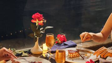 Una mesa dispuesta para una comida, con platos de comida, copas de champán y una vela, con vista a un paisaje urbano de fondo.