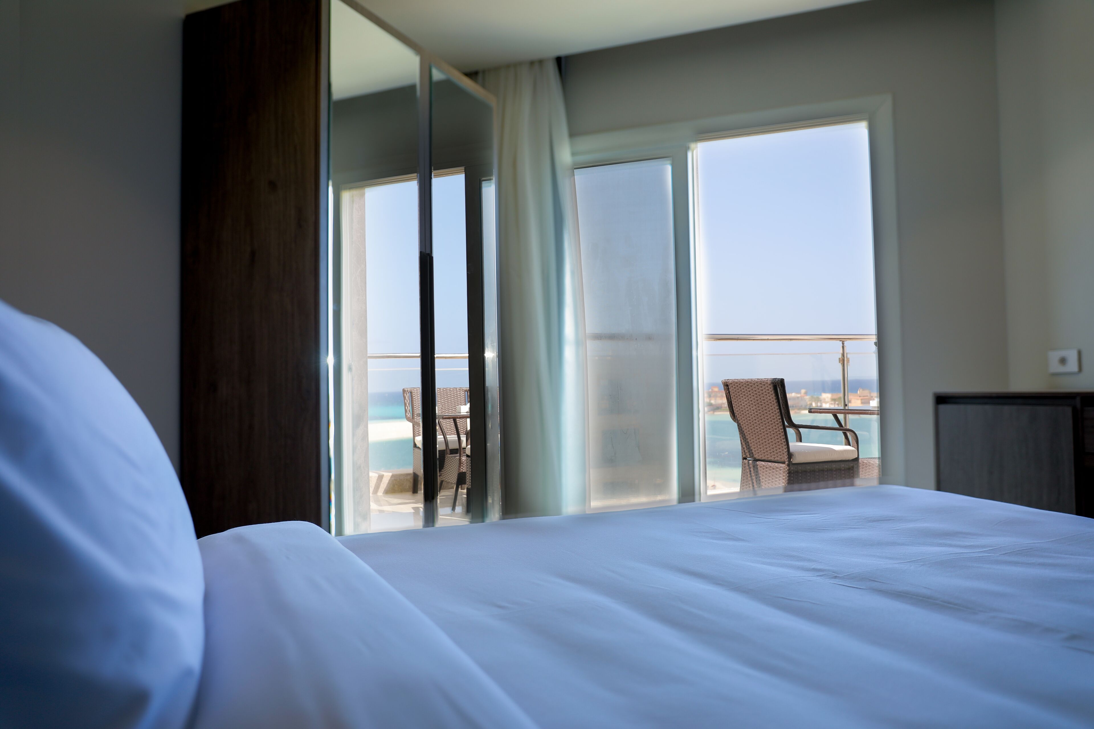 A hotel room with a large bed, a view of the sea through a sliding glass door, and a chair by the window.