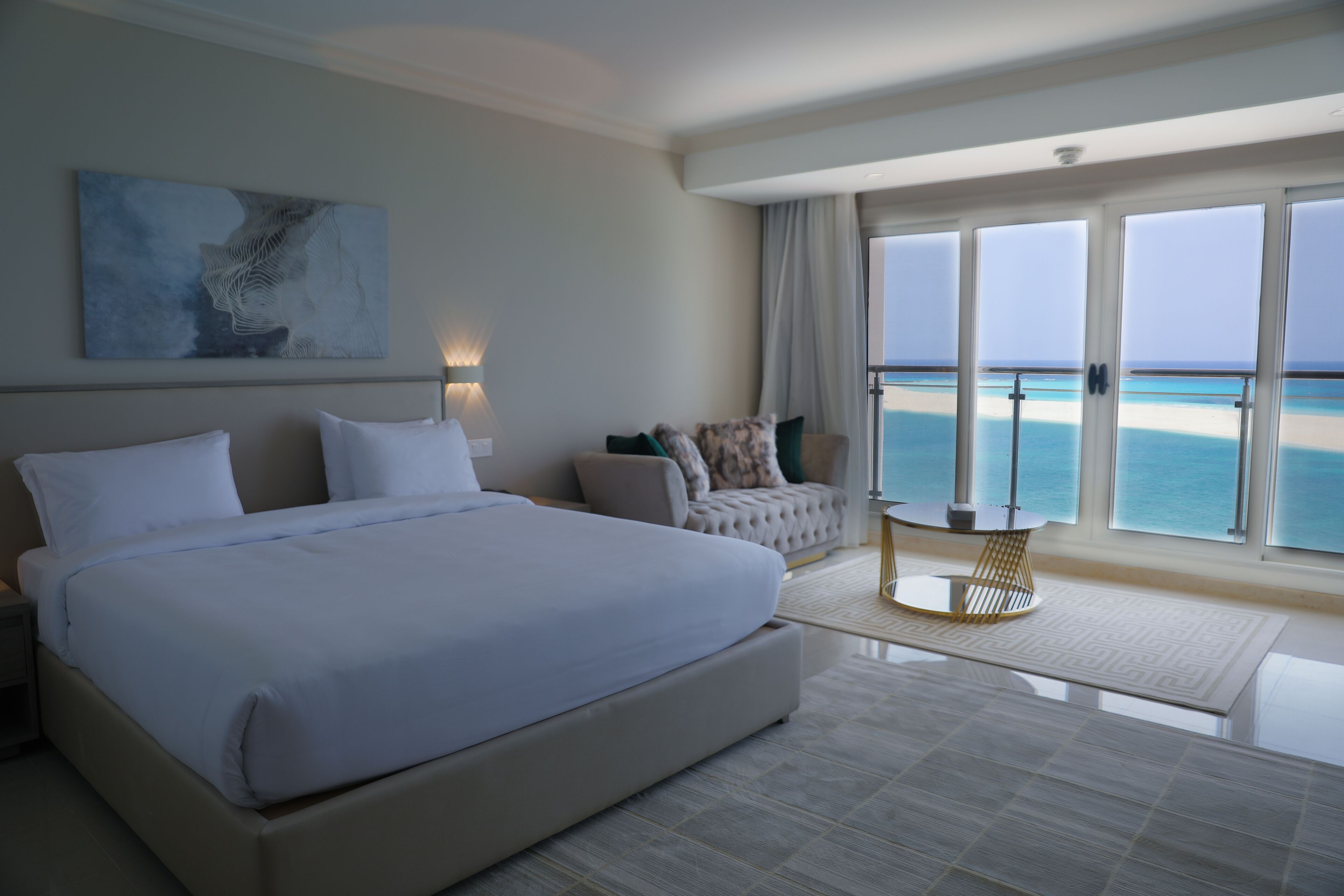A spacious bedroom with a large bed, a seating area with a view of the beach, and a balcony with a glass door.