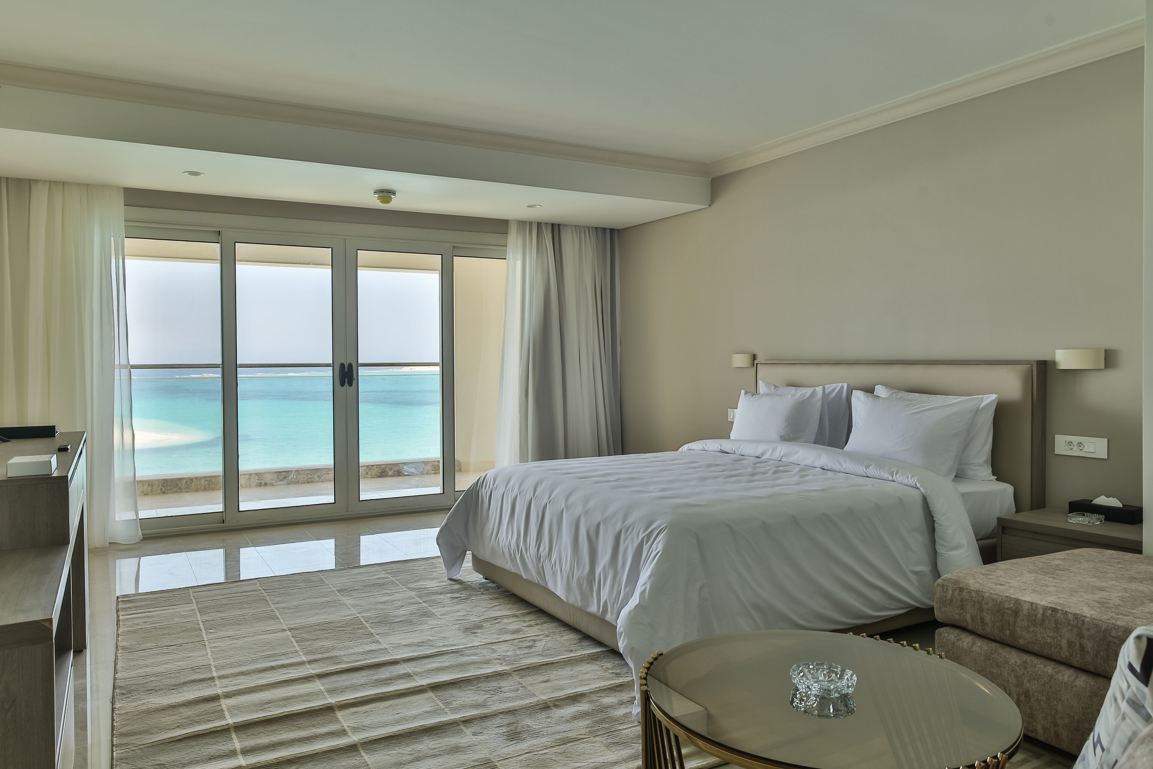 A hotel room with a large bed, a desk, a chair, and a view of the ocean.