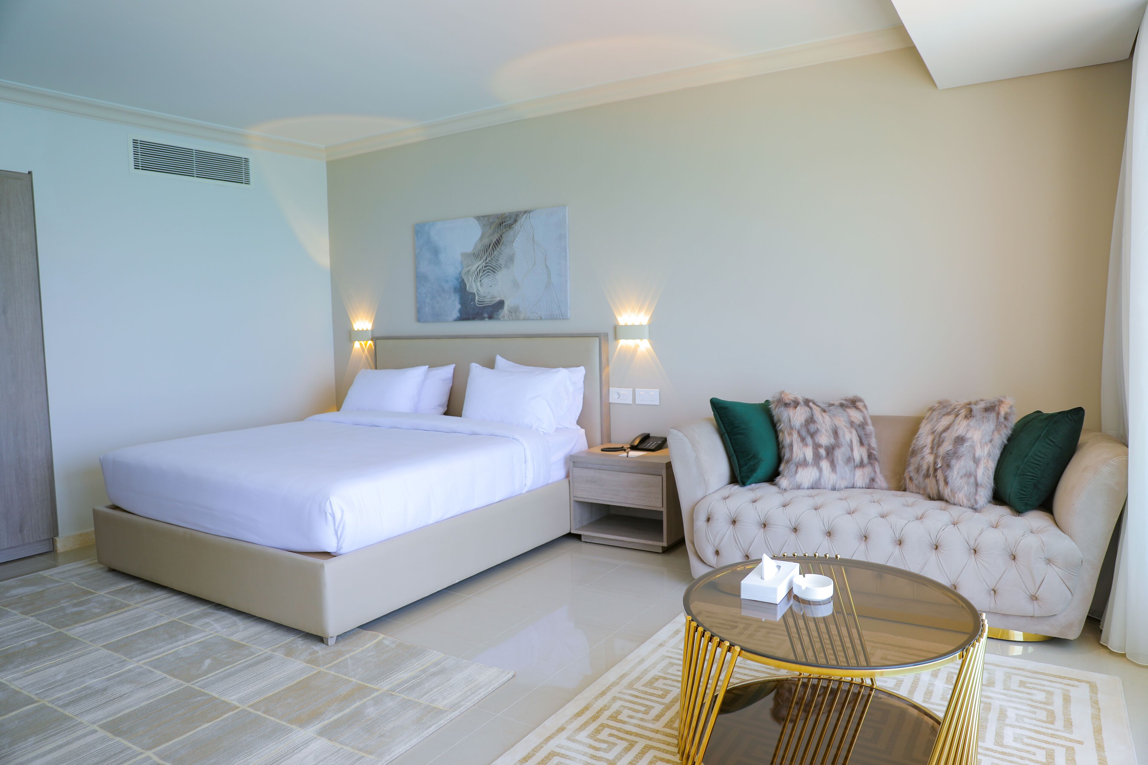 A hotel room with a large bed, a sofa, a coffee table, and a painting on the wall.
