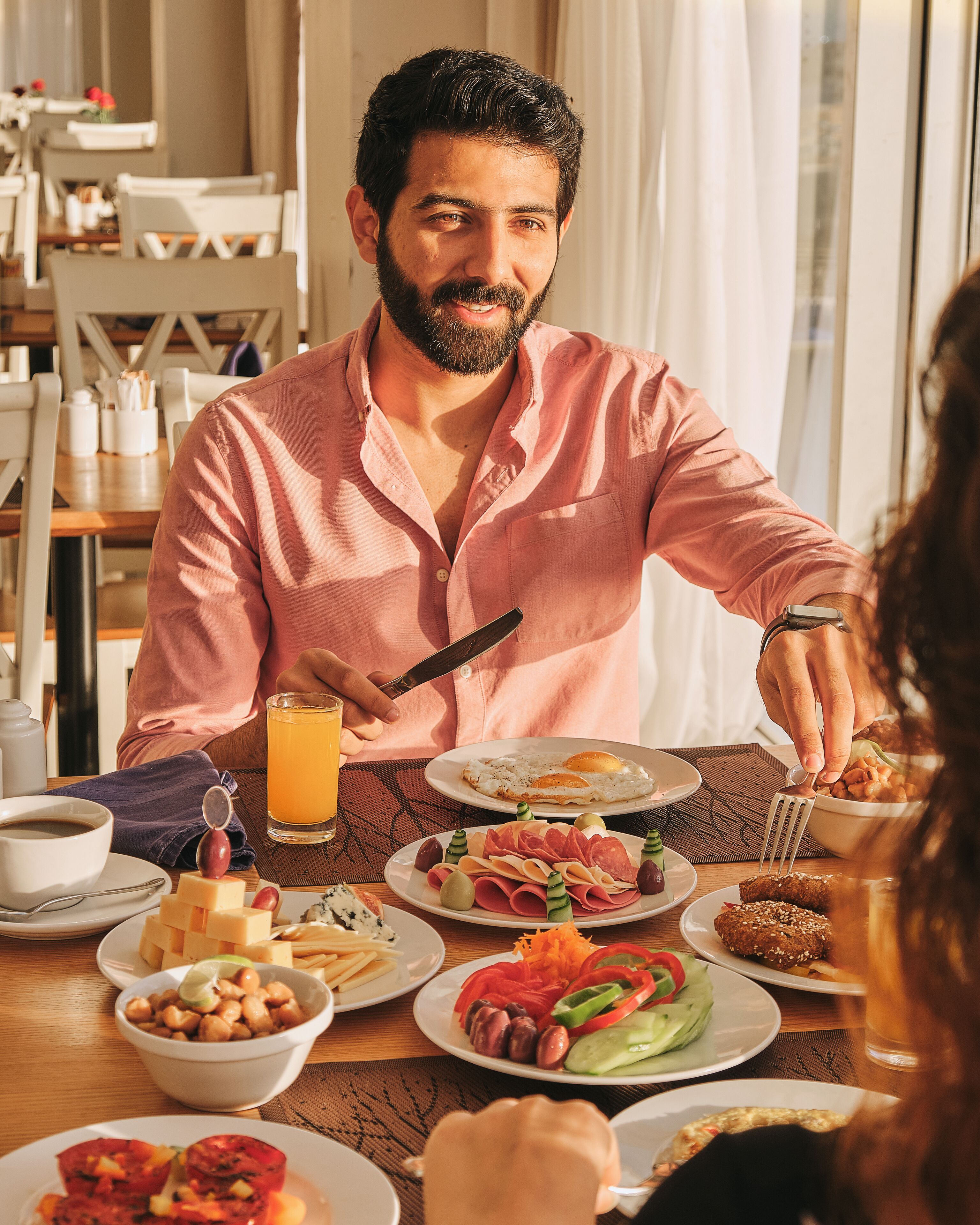A breakfast setting with a variety of dishes including eggs, meats, and vegetables, and a person using a fork.