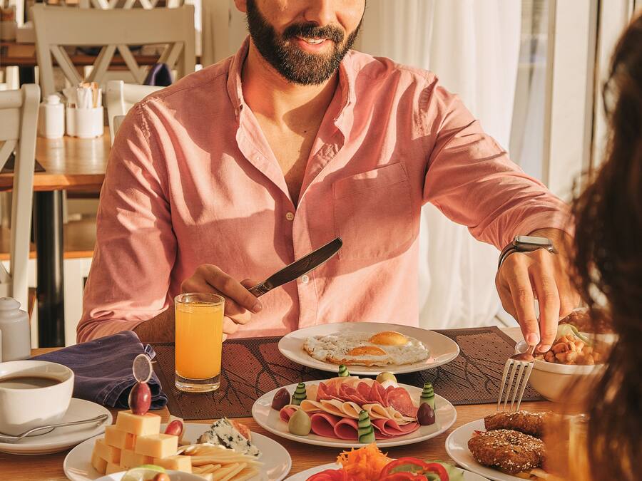 A breakfast setting with a variety of dishes including eggs, meats, and vegetables, and a person using a fork.