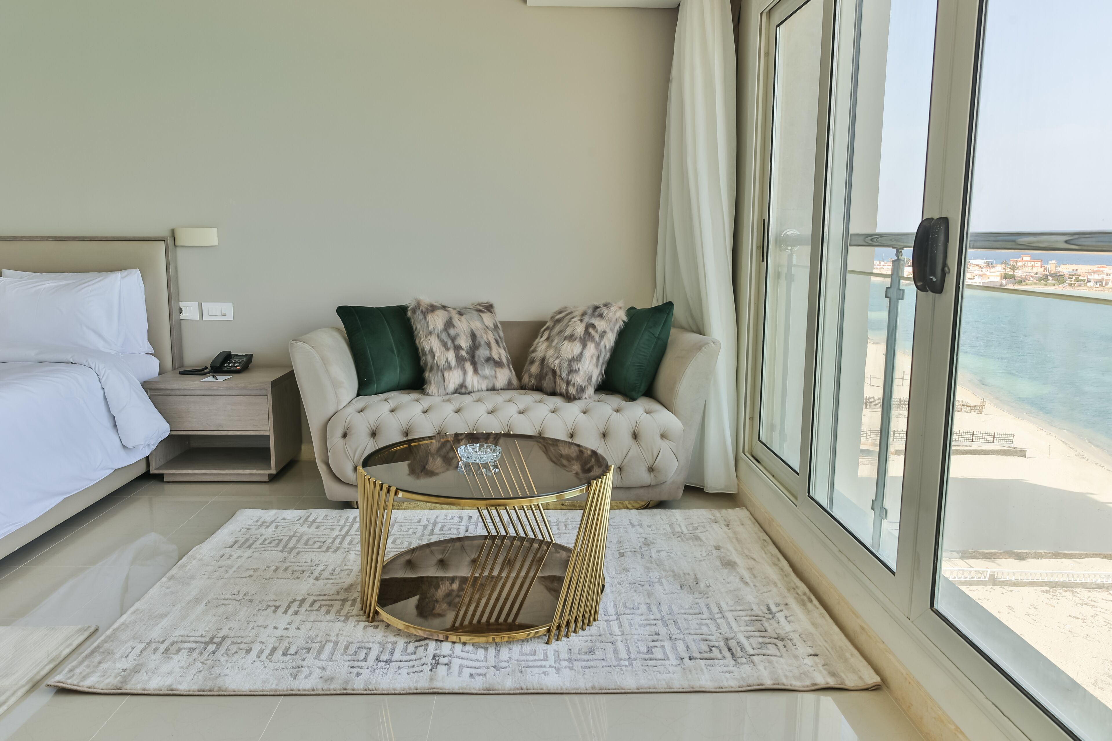 Una camera d'albergo con un letto, un divano, un tavolino in vetro, un comodino e vista mare.