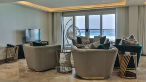 Ein modernes Wohnzimmer mit einem großen Fenster und Meerblick, zwei Sofas, einem Fernseher und Dekorationselementen.