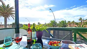 A table with a bottle of Campo Viejo Rijo wine, a glass of red wine, a bowl of fruit, and a green plant in a pot.