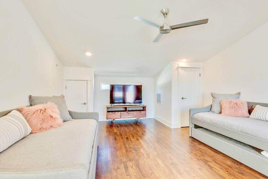Ein geräumiges Wohnzimmer mit hohen Decken, einem Deckenventilator und einem Fernseher auf einem Holzständer.