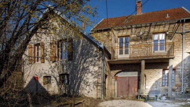 Una casa de piedra de dos plantas, con balcón, garaje y patio cercado.