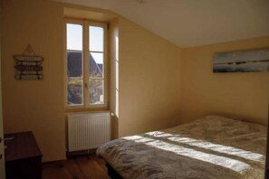 A bedroom with a bed, a window, a radiator, and a wall-mounted picture.