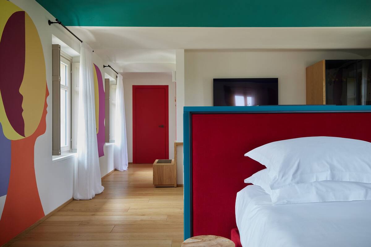 Une chambre d’hôtel avec un plancher en bois, une porte rouge, une télévision et un lit avec une literie blanche.